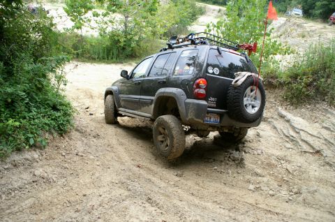 2006 Jeep Liberty - A black 2006 Jeep Liberty navigates a challenging dirt trail, equipped with a roof rack and spare tire, its off-road capabilities.