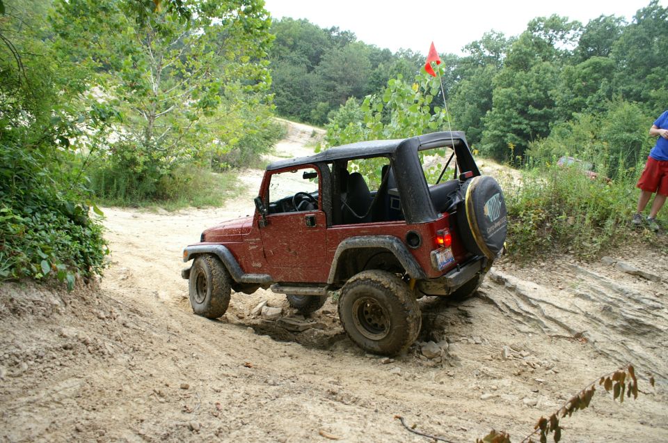Red Jeep Wrangler navigating a dirt trail with large tires. Orange flag on a pole in the background