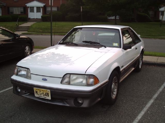 White 1989 Ford Mustang GT parked in a lot. License plate is MLG-64N