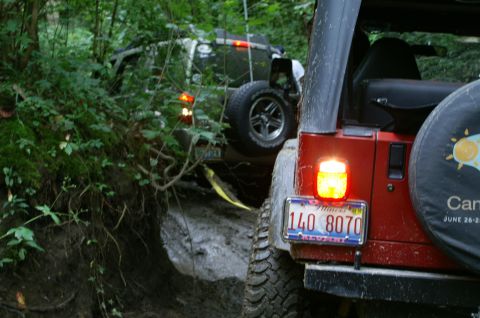2006 Jeep Liberty - Two Jeeps navigate a challenging, muddy path through dense woods.