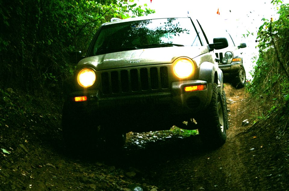Silver Jeep Liberty on a dirt path, front view. Another Jeep is visible behind it