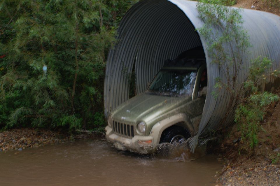 Green Jeep Liberty driving through a large metal culvert with water splashing