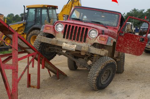 2006 Jeep Liberty - Mud-covered red Jeep Wrangler attempting an obstacle course with a backhoe in the background.