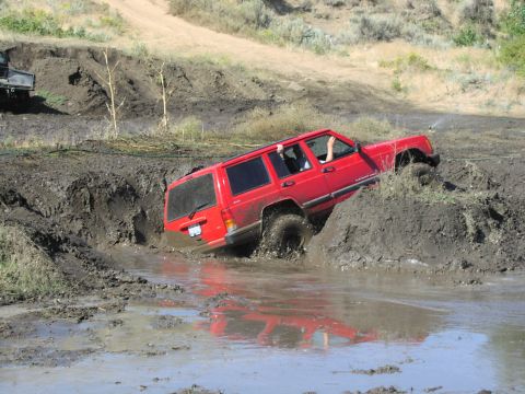 1979 Ford Bronco - A red Jeep Cherokee navigates a challenging mud obstacle, with another vehicle in the background.