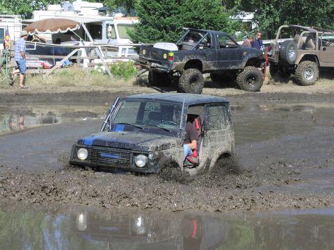 1979 Ford Bronco - Off-road vehicles navigate a challenging muddy course, kicking up spray as they go.
