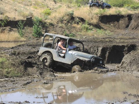 1979 Ford Bronco - Two people navigate a muddy obstacle course in a Jeep Wrangler.