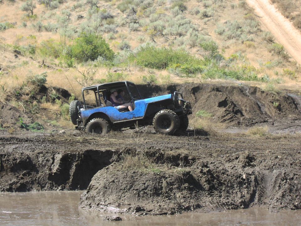 Blue off-road jeep with roll cage driving through mud
