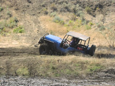 1979 Ford Bronco - A blue off-road vehicle navigates a muddy track on a dry, grassy hillside.