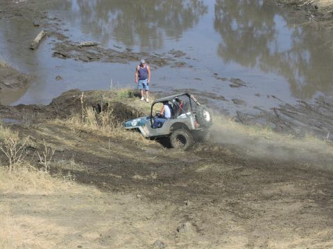 1979 Ford Bronco - A Jeep CJ-7 tackles a challenging muddy incline during an off-road event.