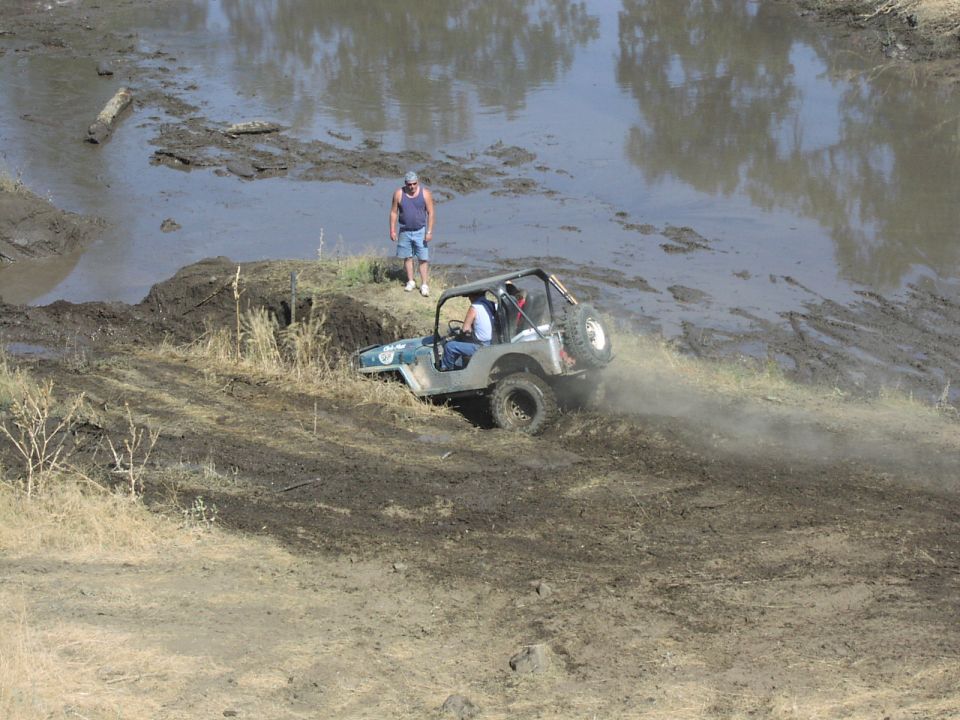Green Jeep CJ-7 navigating a muddy hill, rear-mounted spare tire visible