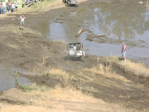 1979 Ford Bronco - An off-road vehicle tackles a muddy obstacle course while onlookers observe the event.
