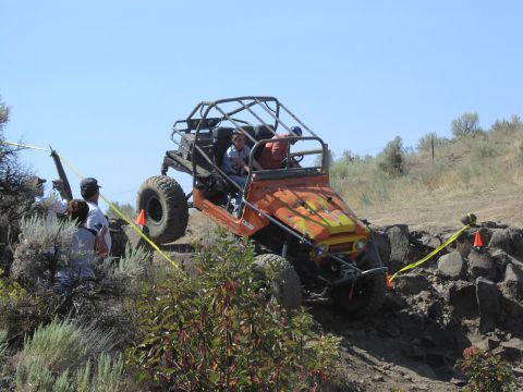 1979 Ford Bronco - An orange off-road buggy navigates a challenging rocky terrain with spectators watching.