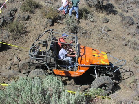1979 Ford Bronco - An orange off-road buggy with a custom roll cage tackles a challenging rocky course, with spectators observing from above.