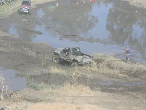 1979 Ford Bronco - A modified pickup truck navigates a challenging mud course, with spectators visible in the distance.