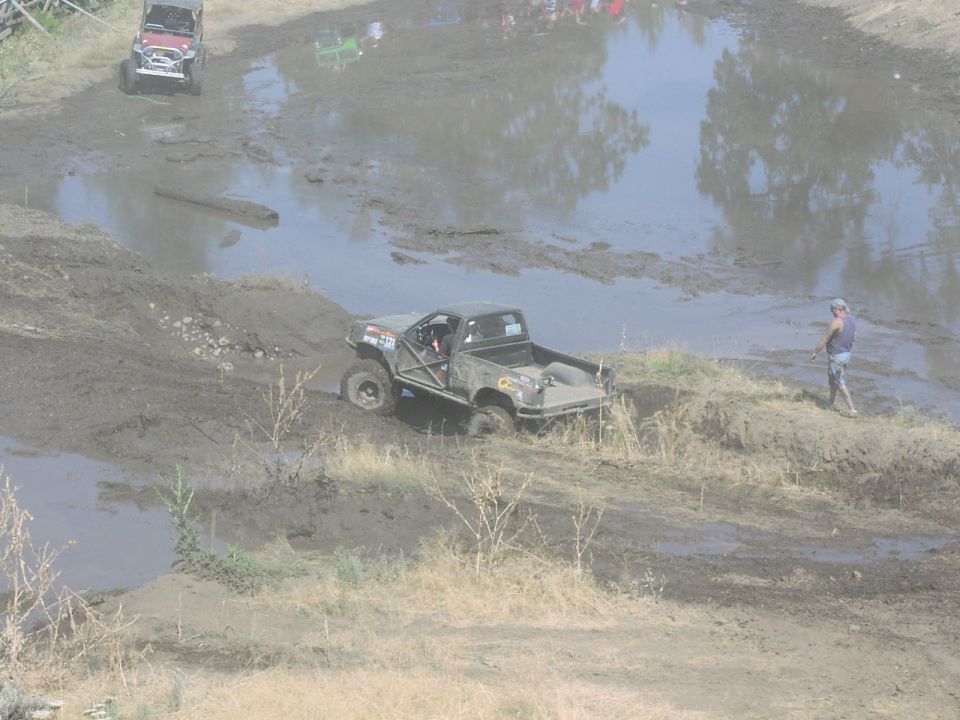 Muddy pickup truck with roll cage going through a mud pit, another Jeep in background
