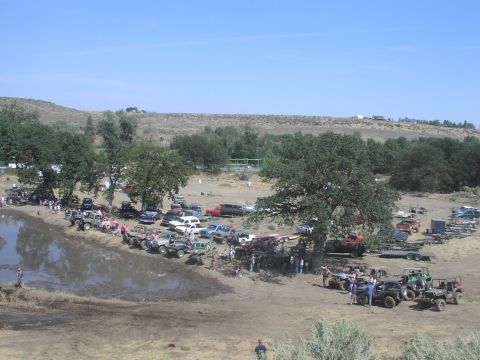1979 Ford Bronco - A large gathering of off-road vehicles and people are seen near a muddy area on a sunny day.