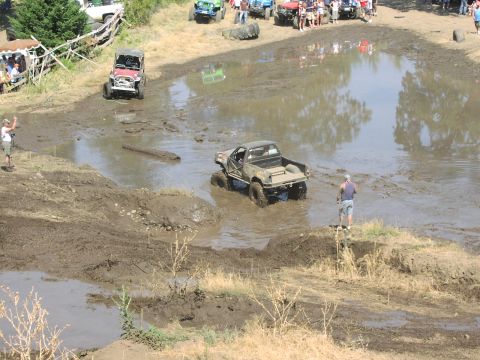 1979 Ford Bronco - A modified pickup truck drives through a muddy water obstacle during an off-road event.