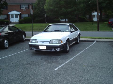 1989 Ford Mustang - A white 1989 Ford Mustang coupe is parked in a lot next to a black car.