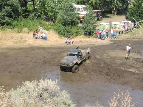 1979 Ford Bronco - A modified pickup truck attempts to drive through a muddy terrain during an event, with onlookers gathered nearby.