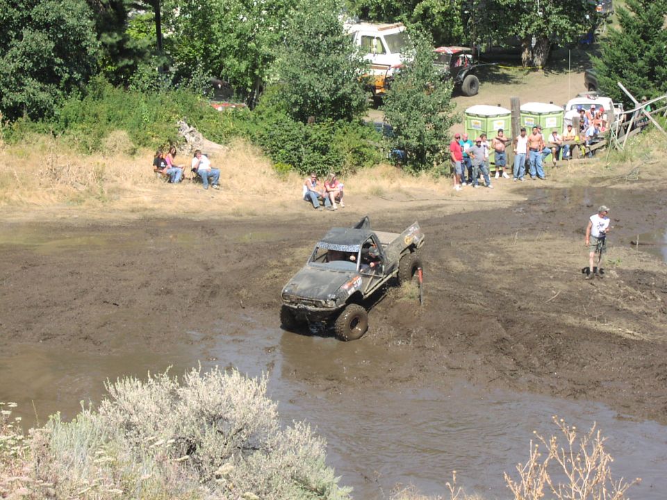 Muddy pickup truck navigating a mud pit with spectators watching