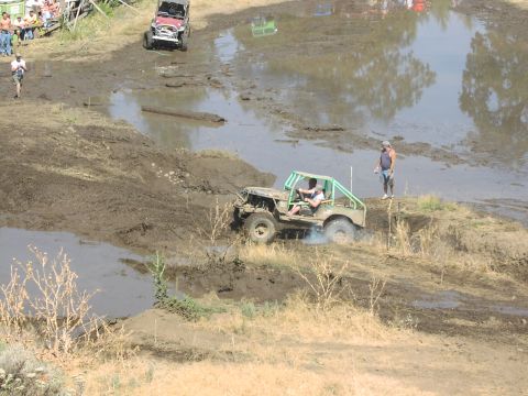 1979 Ford Bronco - Off-road vehicles tackle a challenging mud pit during an event, with onlookers observing the action.