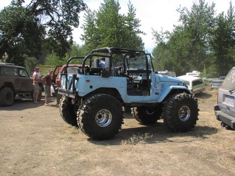 1979 Ford Bronco - Several off-road vehicles are parked on a dirt lot under a canopy of trees.