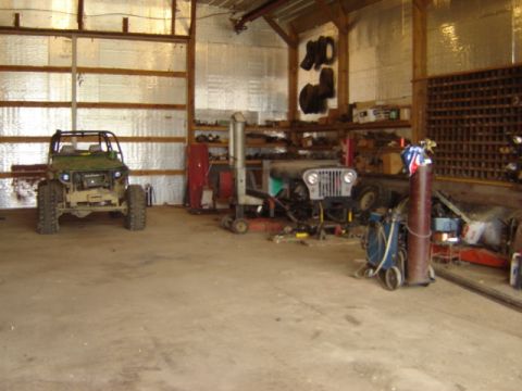 1992 Ford Bronco - A green off-road vehicle is parked in a garage next to a Jeep undergoing repairs.