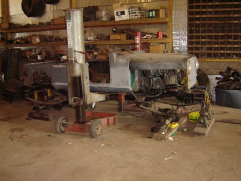 1992 Ford Bronco - Vehicle body and chassis undergoing work on a lift in a cluttered garage setting.