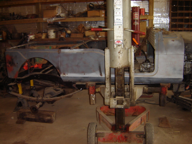 Jeep CJ-5 body, stripped down and on a lift in a garage. The rear axle is visible underneath