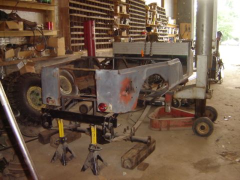 1992 Ford Bronco - The body of a Jeep CJ-6 is elevated on jack stands in a workshop, undergoing repairs or restoration.