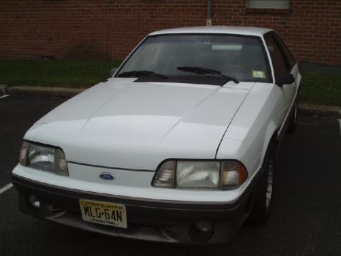 1989 Ford Mustang - A white 1989 Ford Mustang GT is parked in a lot, showing its front end and license plate.