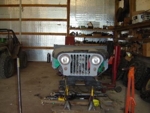 1992 Ford Bronco - Front clip of a Jeep CJ-5 is on a stand in a workshop, with another vehicle to the left.