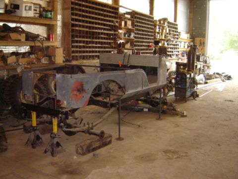 1992 Ford Bronco - The body of a Jeep CJ-6 is elevated on jack stands within a cluttered workshop environment.