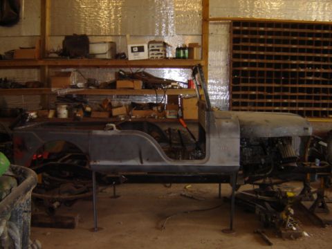 1992 Ford Bronco - The body of a Jeep CJ-6 is seen in a workshop, supported by stands and surrounded by tools and parts.