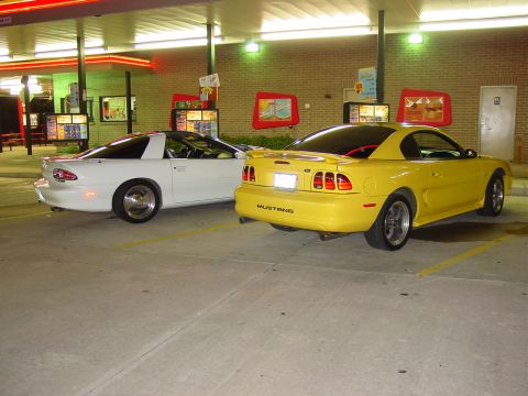 1998 Ford Mustang - Two sports cars, a yellow 1998 Ford Mustang and a white Chevrolet Camaro, are parked at a drive-thru.