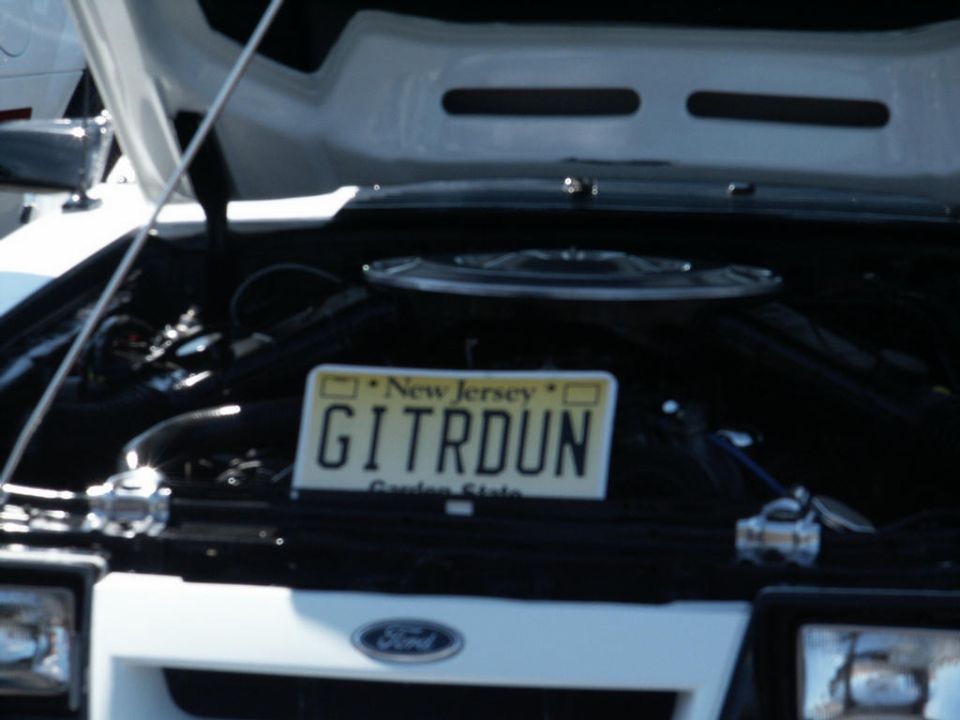 Front of a Ford Mustang with hood open, showing engine and New Jersey license plate that reads GITRDUN