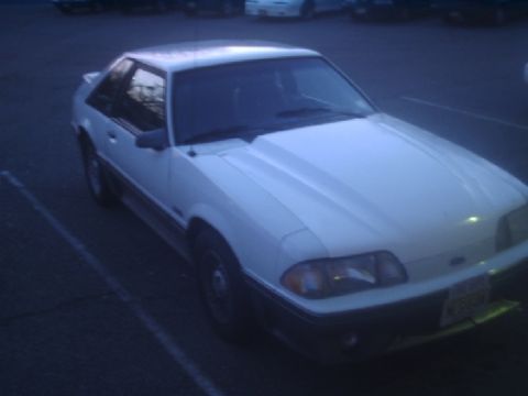 1989 Ford Mustang - A white 1989 Ford Mustang GT coupe is parked in a lot during twilight.