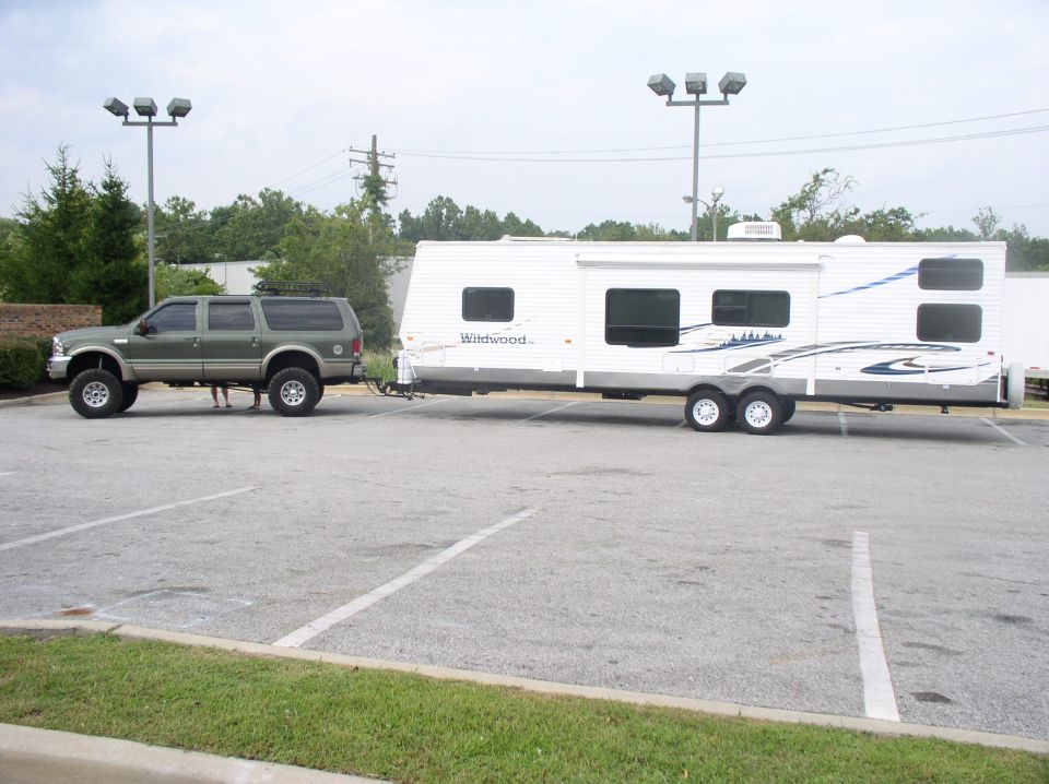 Lifted green Ford Excursion towing a white Wildwood travel trailer in a parking lot