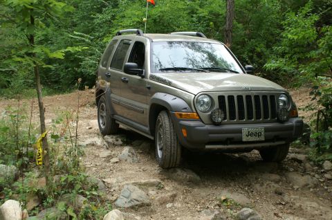 2006 Jeep Liberty - A tan Jeep Renegade navigates a rocky off-road trail with trees and foliage surrounding it.
