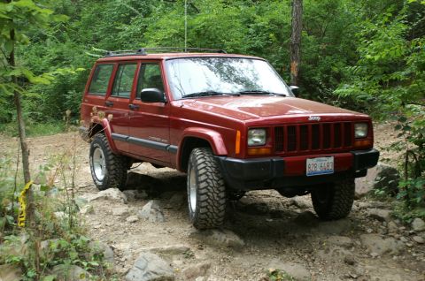 2006 Jeep Liberty - Red Jeep Cherokee XJ navigates a challenging rocky trail, its off-road capabilities. License plate B28 6493 is visible.