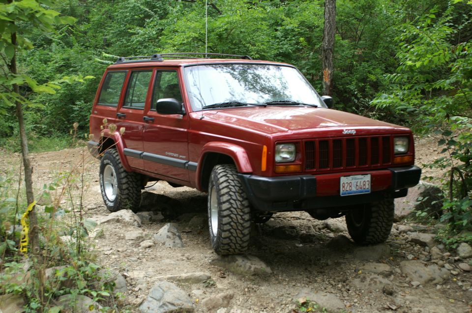 Red Jeep Cherokee XJ with off-road tires on a rocky trail. License plate B28 6493