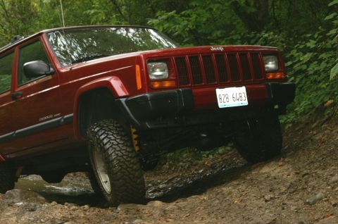 2006 Jeep Liberty - A red Jeep Cherokee XJ navigates an off-road trail with muddy terrain.
