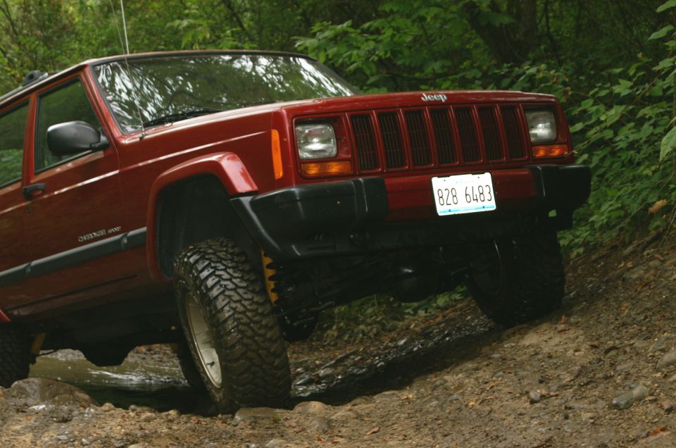Red Jeep Cherokee XJ on a dirt trail, front 3/4 view