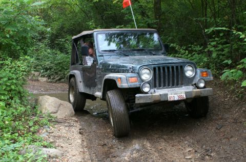 2006 Jeep Liberty - A dark green Jeep Wrangler TJ navigates an off-road trail, its front grille and headlights clearly visible.