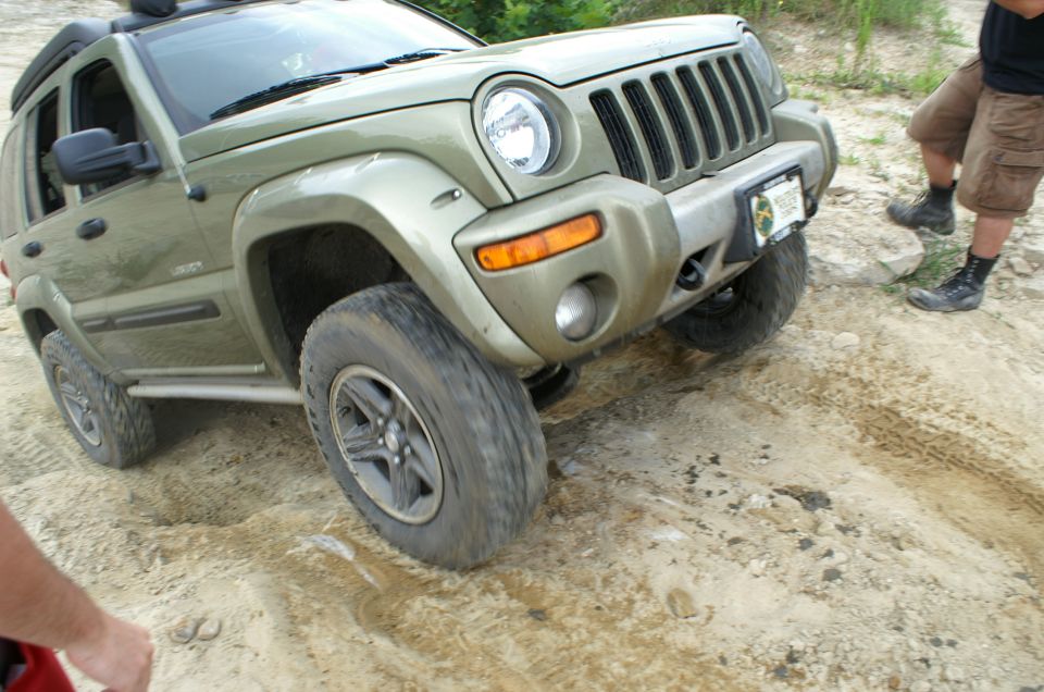 Green Jeep Liberty driving on a dirt trail, front wheel angled up