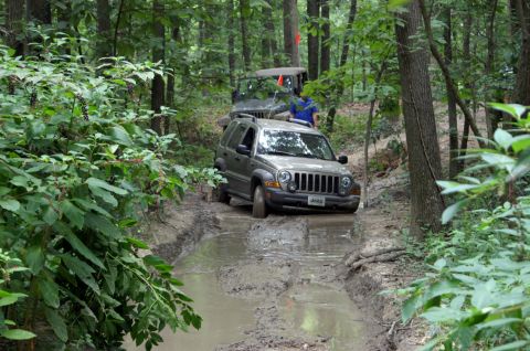 2006 Jeep Liberty - Two Jeeps navigate a challenging muddy path surrounded by dense trees.