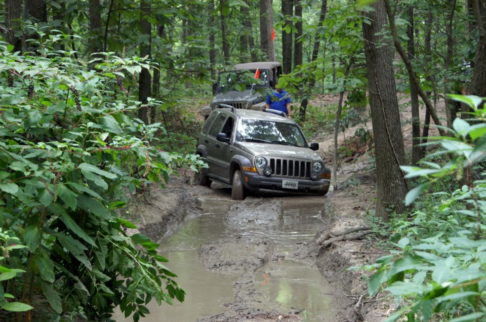 Silver Jeep Liberty driving through a muddy trail in a forest, with another Jeep behind it