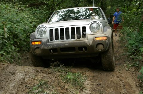2006 Jeep Liberty - A silver Jeep Liberty navigates a muddy off-road trail with a person in the background.