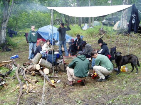 2000 Ford E350 - Campers enjoy an outdoor gathering with a fire and tents set up in a wooded area.