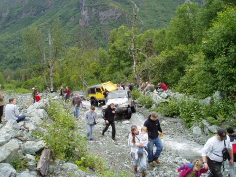 2000 Ford E350 - People and off-road vehicles traverse a challenging rocky terrain in a mountainous, forested environment.